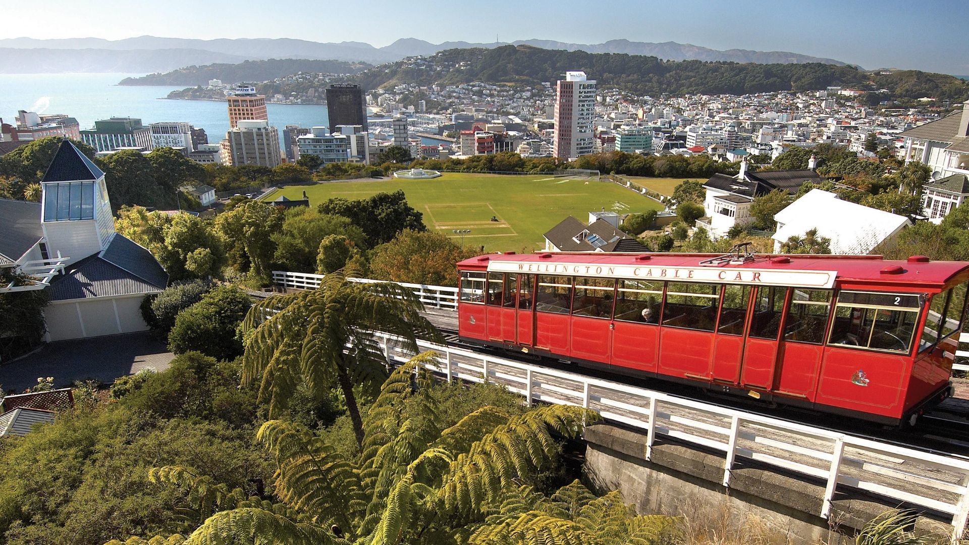 A Red Train On A Track With Wellington Cable Car In The Background